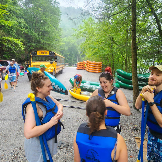 Group of people with life vests on a road near inflatable rafts and a school bus.