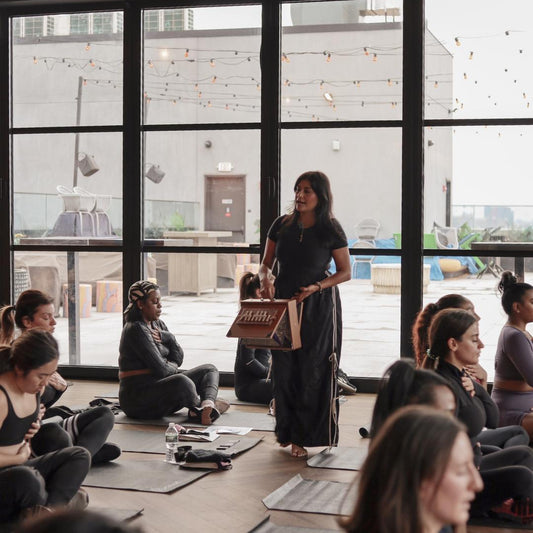 Yogi guiding a group of people in a room with large windows.