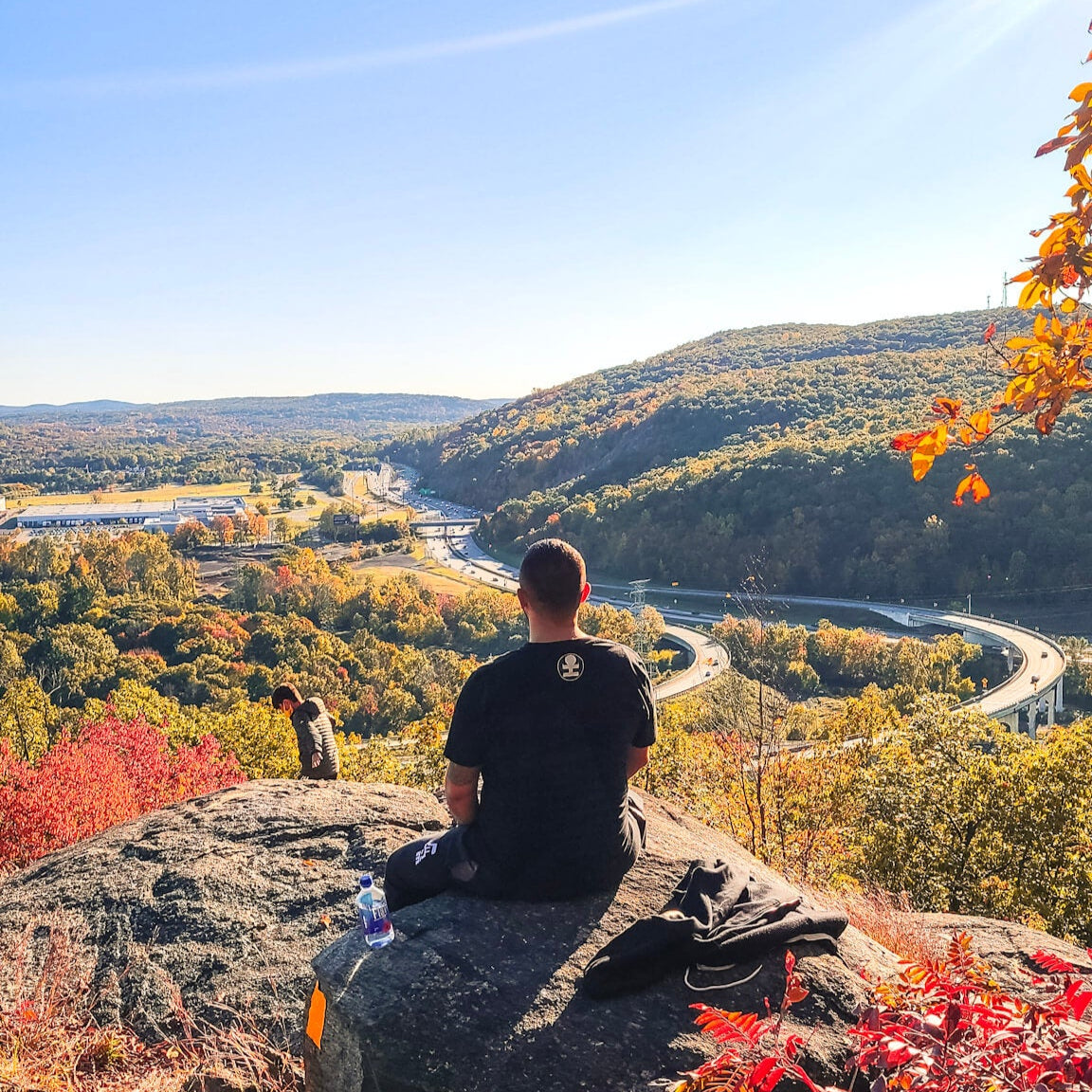Person sitting on a rock overlooking a scenic landscape with autumn foliage.