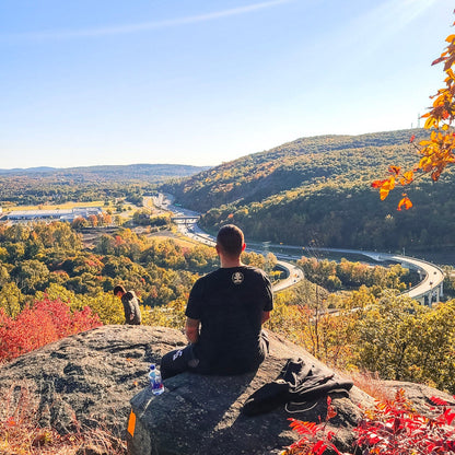 Person sitting on a rock overlooking a scenic landscape with autumn foliage.
