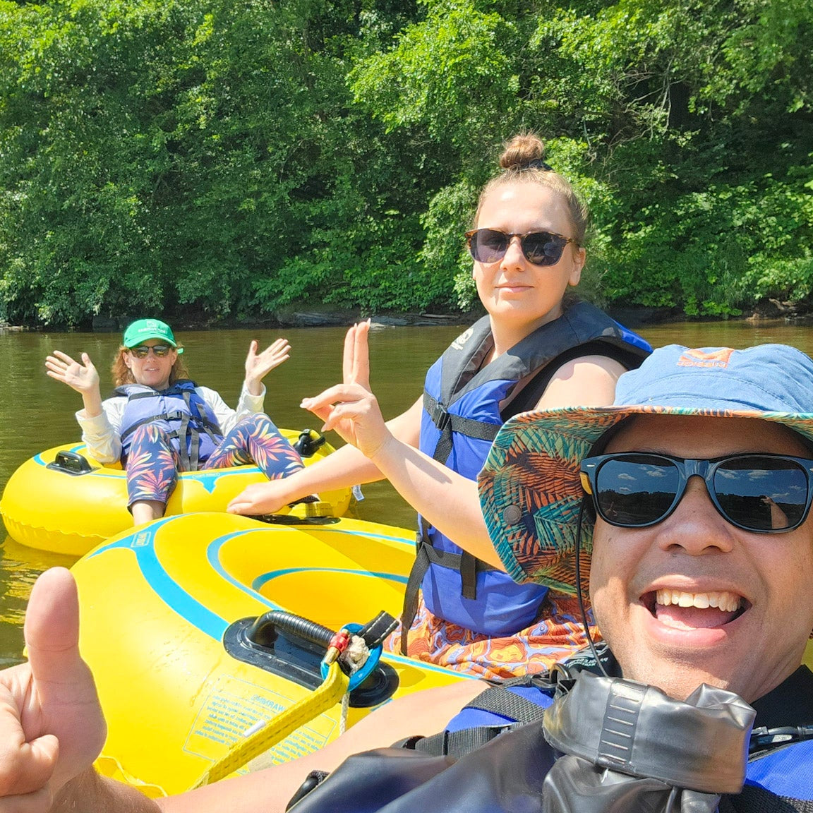 three people on yellow inflatable tubes in a river with trees in the background