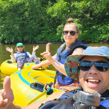 three people on yellow inflatable tubes in a river with trees in the background