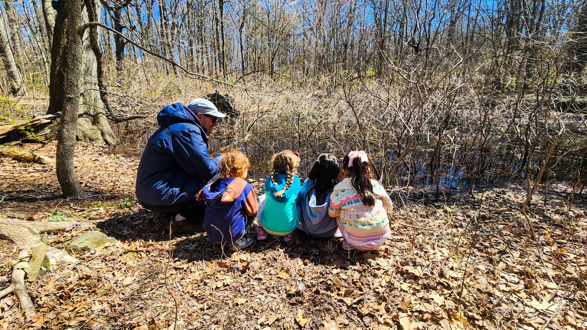 Group of children and an adult sitting on the ground in a forest