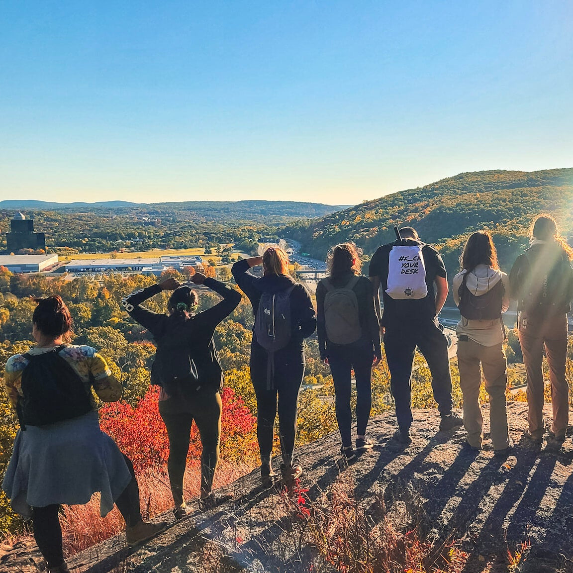 Group of people standing on a rocky outcrop with a scenic view and sunflare.