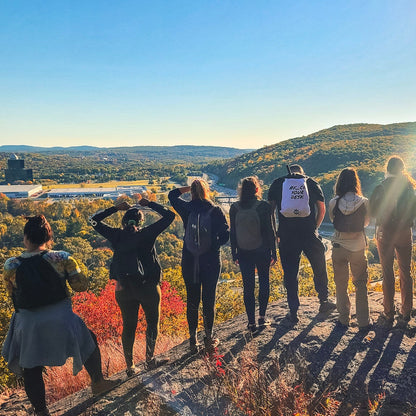 Group of people standing on a rocky outcrop with a scenic view and sunflare.