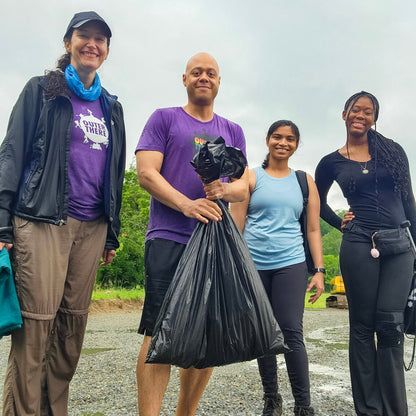 Four people standing outdoors on a rainy day, holding trash bags.