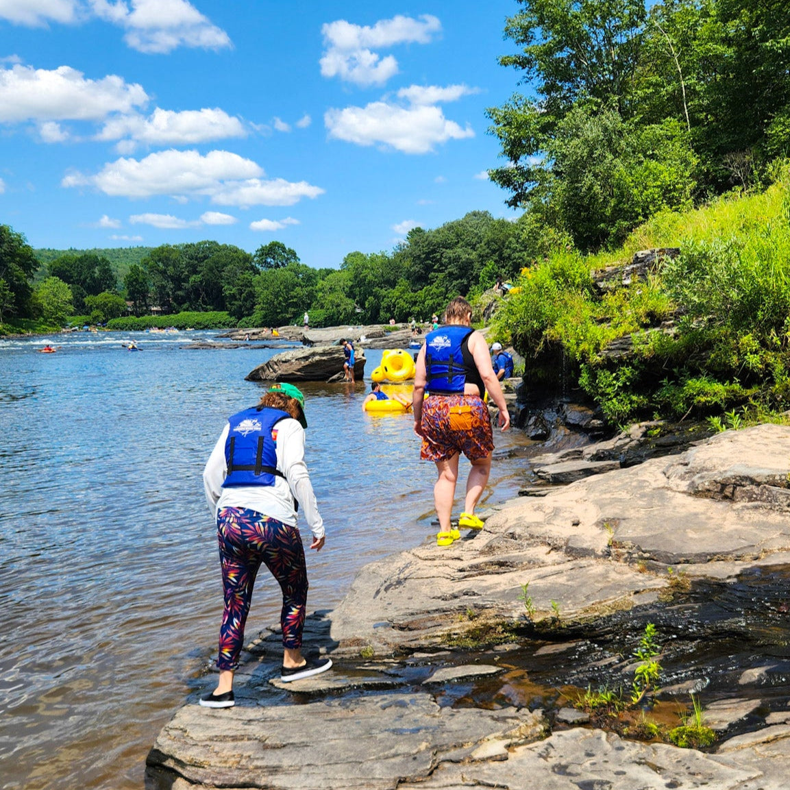 Two people with life vests standing on a rocky riverbank Skinner's Falls Rocky Beach on the Delaware River