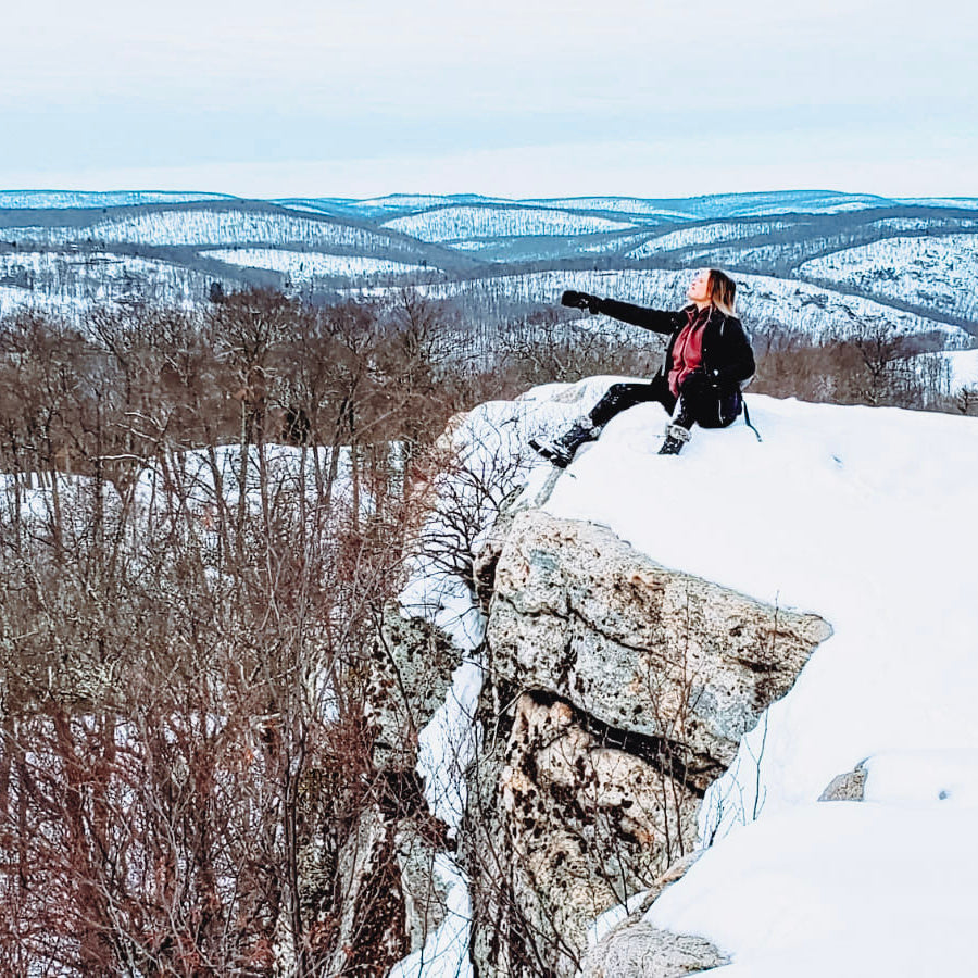 Person standing on a snowy cliff overlooking a vast landscape