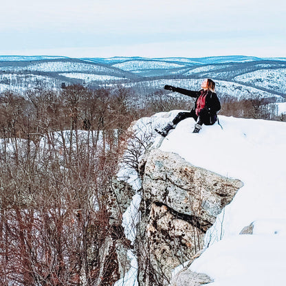 Person standing on a snowy cliff overlooking a vast landscape
