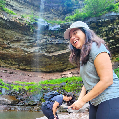 Two women exploring a natural waterfall and pool of water.