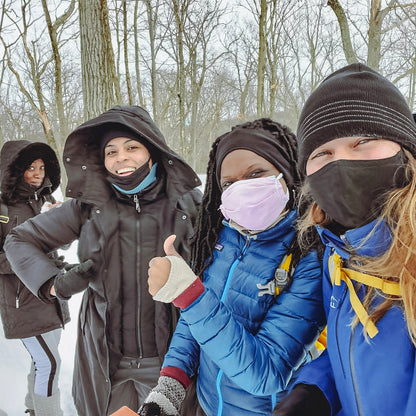 Four people in winter clothing and masks standing in a snowy forest.