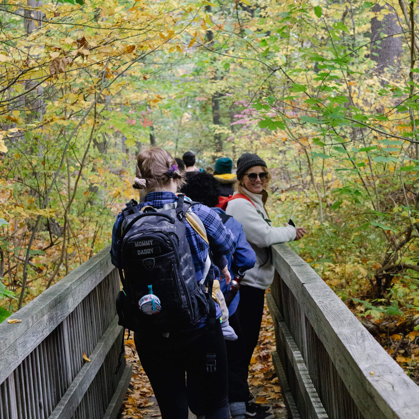 People walking on a wooden bridge in a forest with autumn foliage