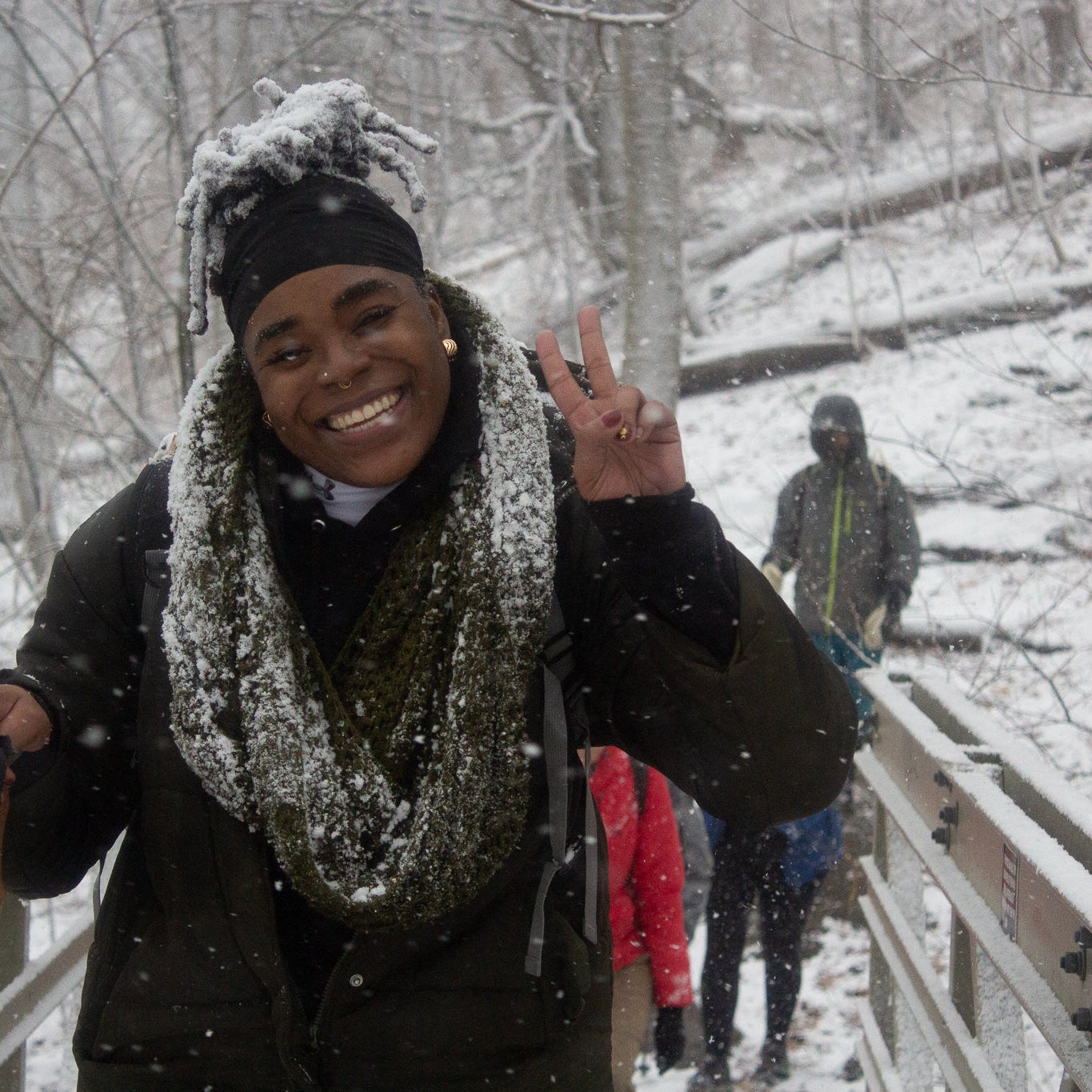 Person in a snowy forest with snow on their hair, wearing a scarf and gloves.