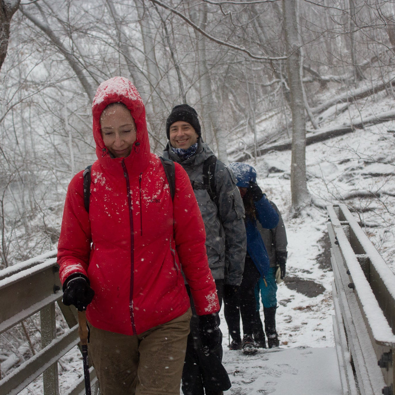 People walking on a snowy path with a person in a red jacket standing out.