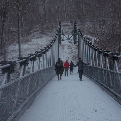 People walking on a snowy suspension bridge in a forest