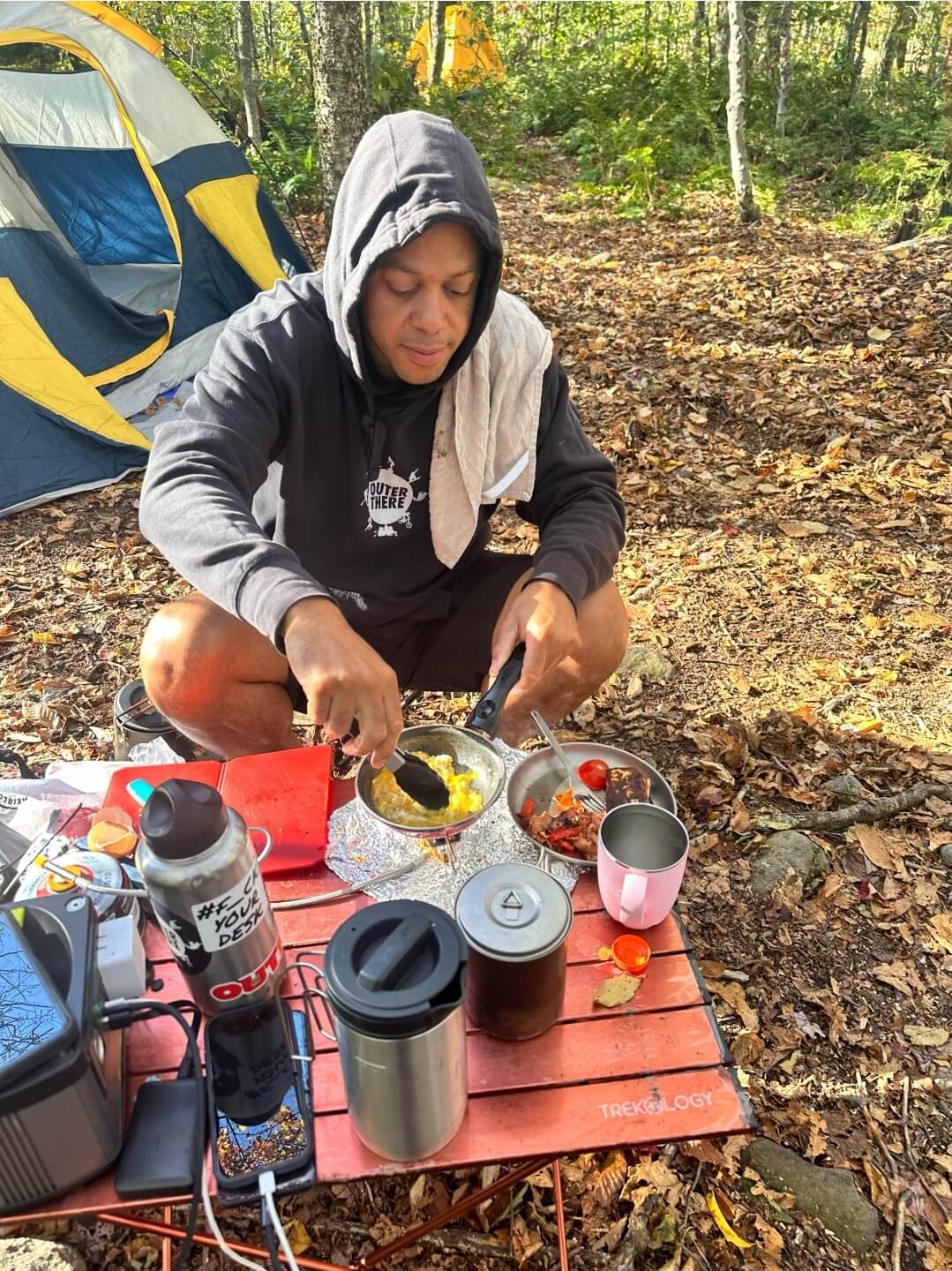 Person camping in the woods, preparing food on a portable stove.
